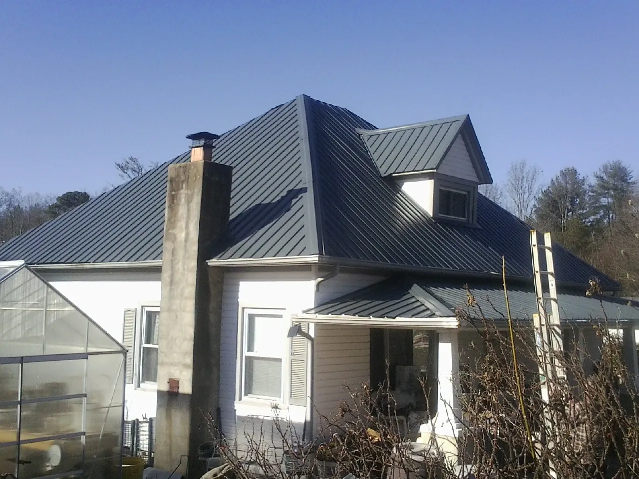 Dark blue standing seam metal roof on a white farmhouse with dormer — Slate & Tile Roof Repair by Roofing Brothers in Maple Grove