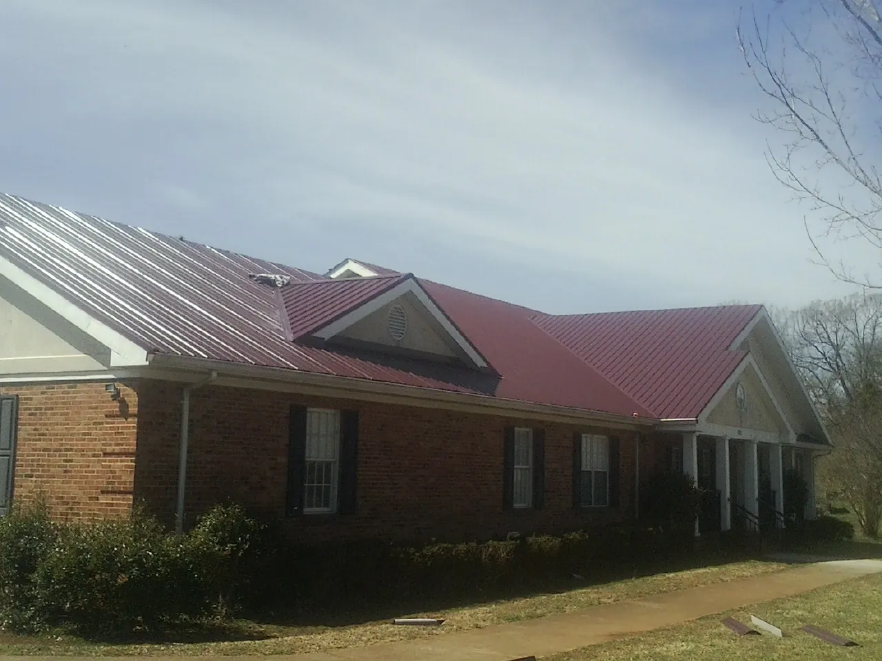 Red metal roof with gabled entries on a long brick building, from a Hail Damage Roof Repair job in Maple Grove