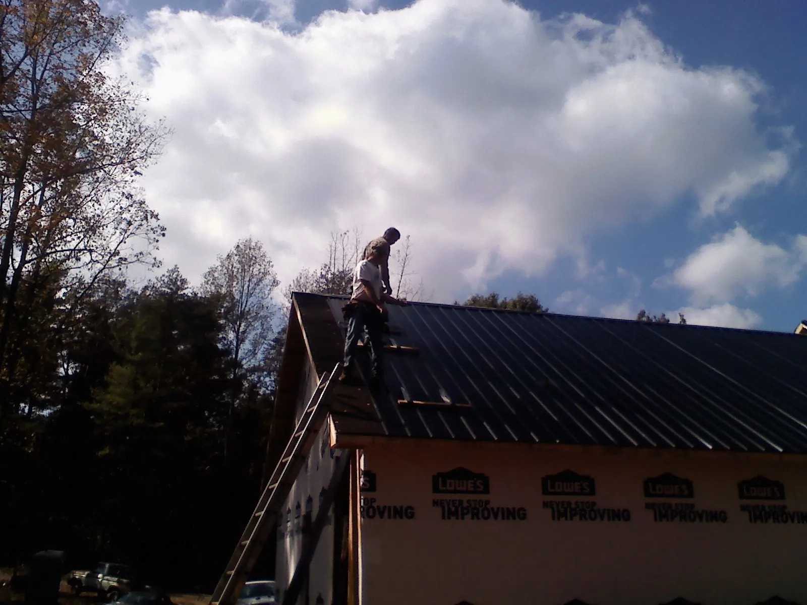 Roofer fastening dark metal panels high against a cloudy sky, from a Roof Inspection job in Maple Grove